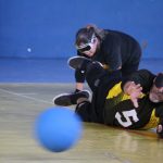 homem praticante de goalball se joga no chão para defender uma bola