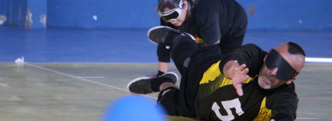 homem praticante de goalball se joga no chão para defender uma bola
