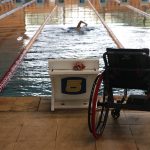cadeira de rodas vazia na beira da piscina, enquanto uma pessoa nada