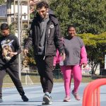 professor Diego Antunes caminha à frente de duas alunas e um aluno, adolescentes e jovens adultos