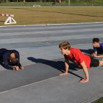 três homens fazem exercício de prancha na pista de atletismo da UFSC